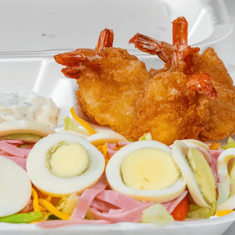 Fried shrimp, hard-boiled eggs, ham, and vegetables in a snack bar salad.